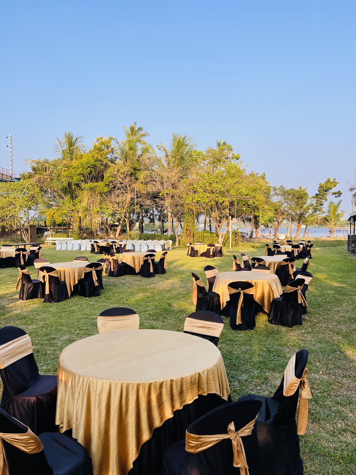 Tables dressed in gold and black on the lawn beside the backwater