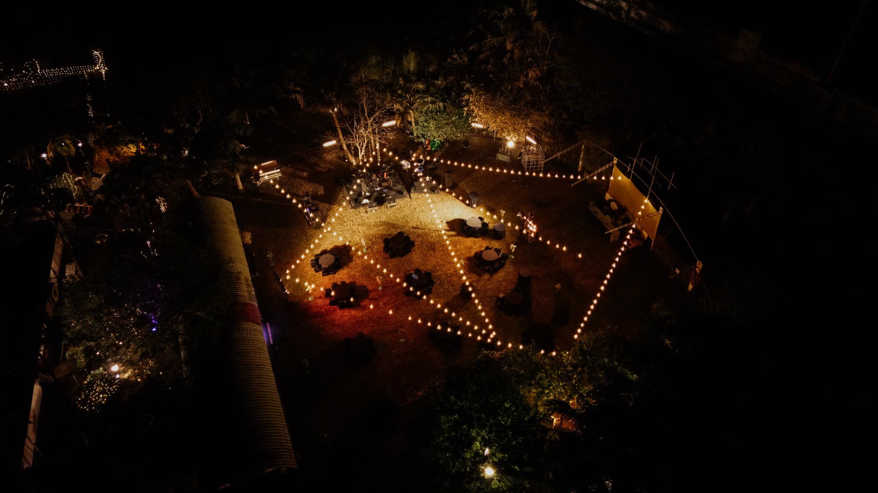 The island lawn at night from above, lined with lights around tables and a stage